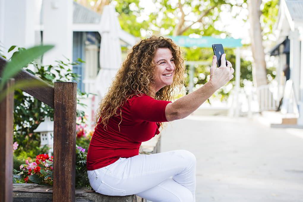 Lisa Monks filming a piece to camera on her phone, sitting outdoors in the sunshine