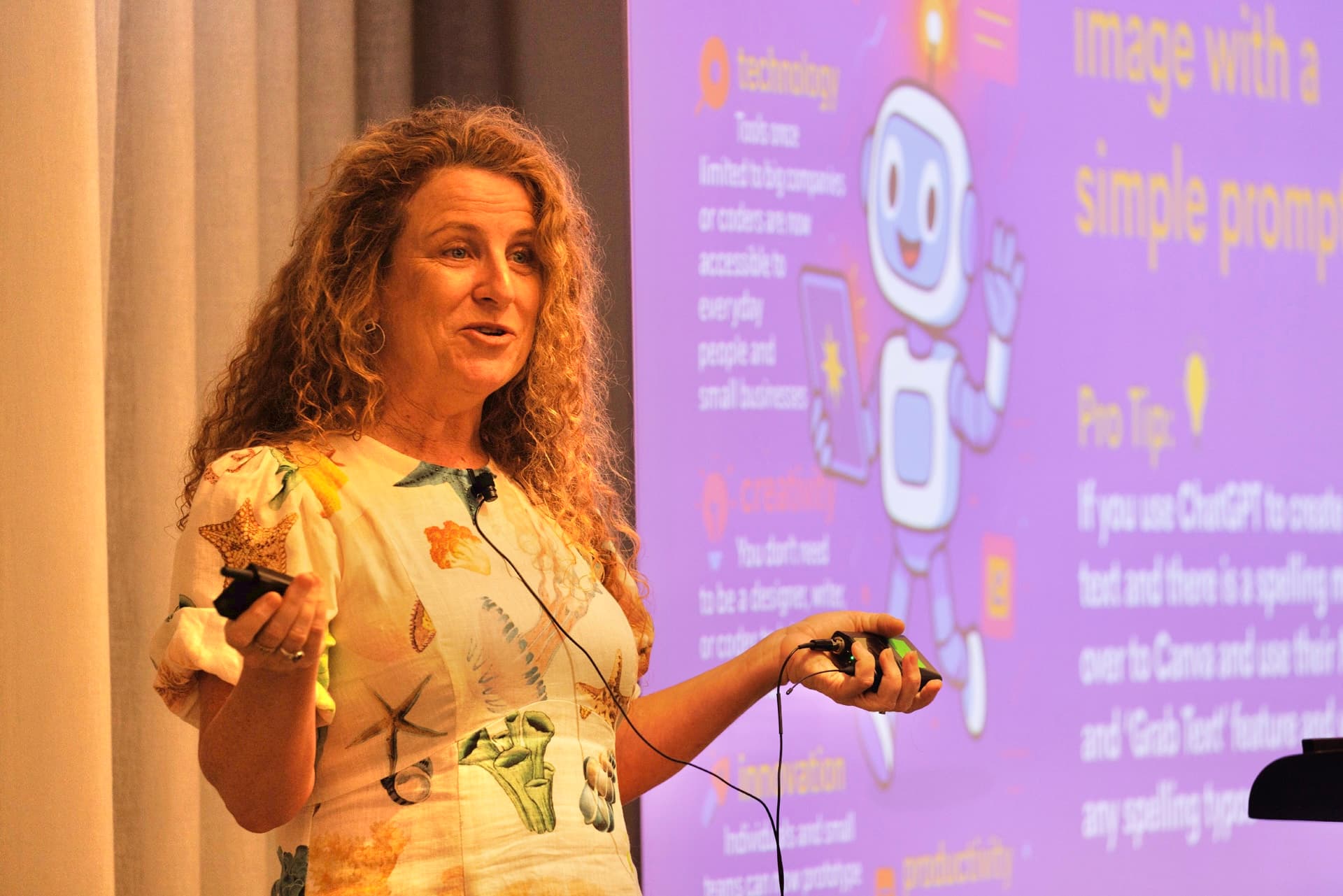 Lisa Monks presenting on stage with a microphone, in front of a slide about AI