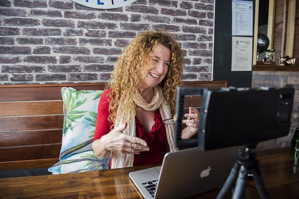 Lisa Monks explaining something on a video call, seated at her laptop in a café